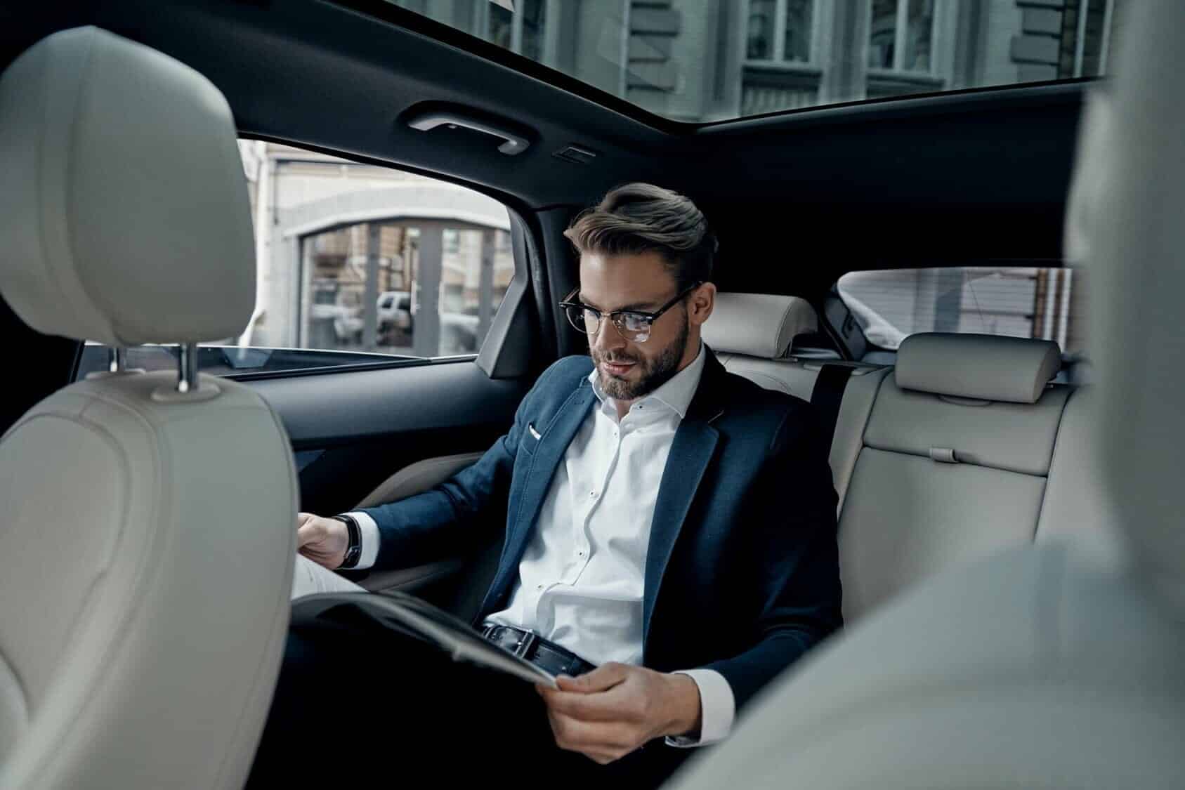 Businessman sitting in the back of a luxury vehicle reading a publication